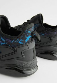 Black athletic shoes feature a textured upper with blue and purple splatter patterns. Rounded heel and contrasting black sole with a grip texture.