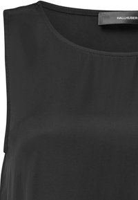Svart ärmlös blus med rund halsringning, tillverkad av slät tyg. Har en subtil lyster och en etikett på baksidan med "HALLHUBER."