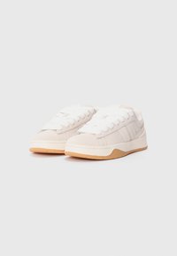 Beige canvas sneakers with textured suede accents, featuring a padded tongue and white laces, complemented by a brown rubber sole.