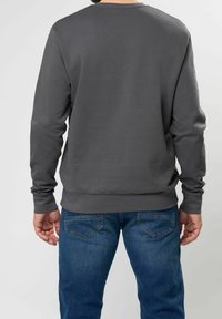 Sudadera gris de cuello redondo con mangas largas, textura suave, puños acanalados y dobladillo ajustado, combinada con jeans de mezclilla azul.