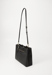 Sac à main en cuir noir à la forme structurée, avec des détails en zip doré, une bandoulière longue réglable et deux poignées supérieures. Texture lisse, accents minimaux.