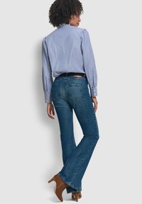 Jeans a campana in denim blu con un lavaggio sbiadito, design a cinque tasche e cuciture rinforzate. Abbinati a una camicia a righe blu e bianche con bottoni.