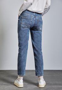 Blå denimjeans med rak bendesign, med två bakfickor och en avslappnad nederkant. I kombination med vita sneakers och lätta strumpor.