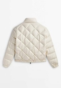 Veste matelassée crème avec coutures en forme de losange, col montant, poignets élastiqués et ourlet court avec une petite languette noire.