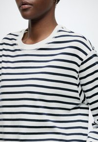 Fehér és tengerészkék csíkos hosszú ujjú ing, kerek nyakkivágással, puha pamut anyagból és finom varrási részletekkel.