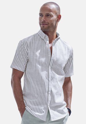 Man wearing a short-sleeve, white and gray vertical striped button-up shirt with hands in pockets, looking slightly to the side.