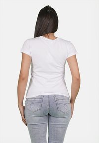 T-shirt bianco a maniche corte con scollatura rotonda, forma aderente e texture liscia, indossato con jeans skinny blu chiaro con tasche posteriori.