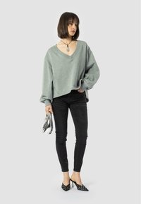 Maglione grigio oversize a scollo a V, jeans skinny neri, tacchi neri con borchie e borsa argentata. Tessuto morbido con silhouette casual e dettagli.