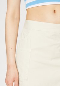 Jupe couleur crème en coton avec une texture lisse, dotée d'une poche latérale et d'un design simple.