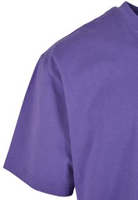Tricou din bumbac violet cu mâneci scurte, decolteu rotund și o textură fină. Prezintă un detaliu de cusătură subtil pe margine.
