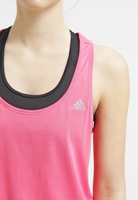 Rosa atletisk linne tillverkat av ett slätt material med ett svart innerlager, rund halsringning och en liten Adidas-logotyp i silver.