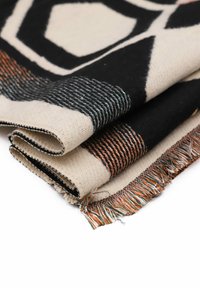 Tessuto intrecciato con motivi geometrici nei toni del nero, crema e arancione. I bordi sono frangiati con dettagli di filo multicolore.