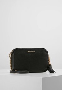 Zwarte leren crossbodytas met een gladde textuur, gouden details, kettingriem en decoratieve kwast. Voorzien van logo aan de voorkant.