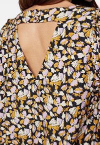 Blusa nera in tessuto con un motivo floreale in viola, giallo e bianco. Il design presenta un'apertura a forma di V sul retro.