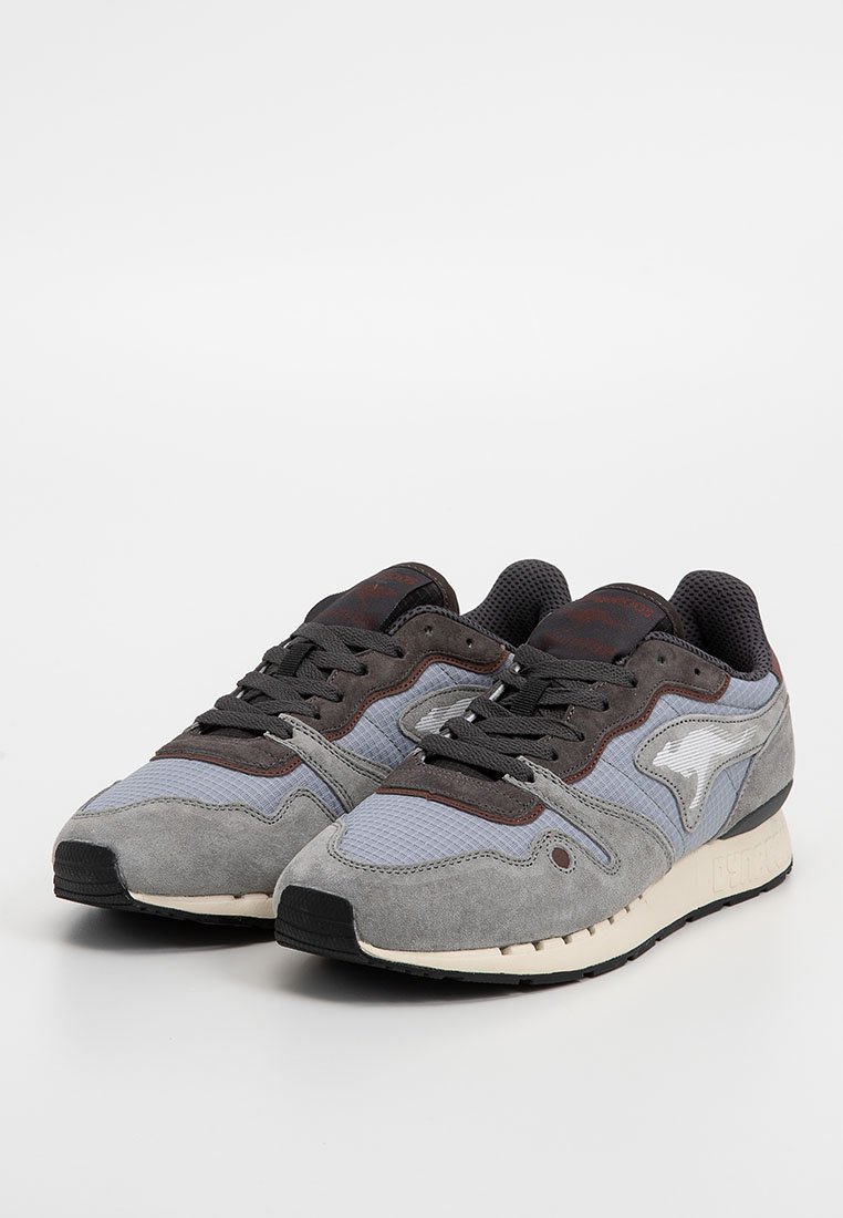Een paar grijs en zwarte sport sneakers met mesh en suède details, een witte zool en zwarte veters op een witte achtergrond.