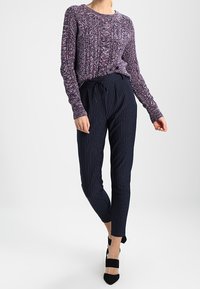 Maglione a maglia testurizzata viola abbinato a pantaloni tapered navy a righe, con vita regolabile e scarpe nere con tacco alto.