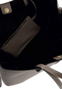 Otwarta torebka typu tote w kolorze taupe z dopasowaną zamykaną na zamek kosmetyczką w środku, czarnym wnętrzem oraz złotym zapięciem na magnes.
