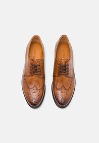 Scarpe in pelle marrone caratterizzate da un design brogue, finitura lucida e perforazioni decorative; lacci piatti e punta arrotondata.