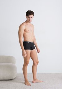 Schwarze, kurze Unterwäsche mit einem Bund, der das Logo "Calvin Klein" trägt. Der Stoff sieht glatt aus und schmiegt sich eng an die Haut.