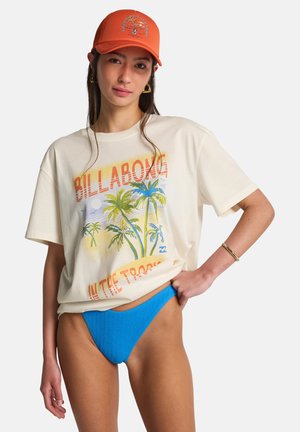 T-shirt grafica color crema con stampa di palme e testo "BILLAONG", abbinata a slip bikini blu brillante con texture e a un cappellino arancione.
