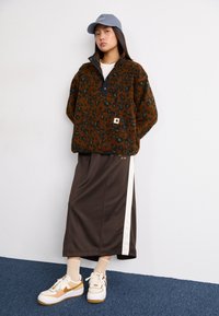 Pull en polaire marron avec imprimé léopard, col snap noir, jupe longue marron avec une rayure blanche, baskets blanches avec des accents beige et gomme.