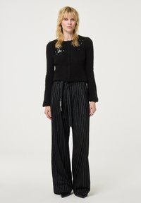 Zwarte gebreide cardigan met ronde hals en knopen, gecombineerd met zwarte, wijde broek met krijtstreep, voorzien van een ceintuurdetail.