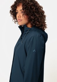 Marineblau leichte, wasserdichte Jacke mit Kapuze, Reißverschlüssen und Kordeln. Verfügt über ein elegantes Design und dezente Logo-Akzente an den Ärmeln.