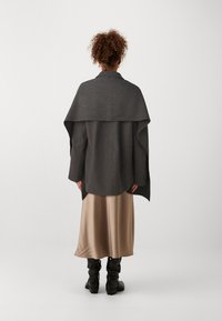 Palton supradimensionat din amestec de lână gri cu design drapat, asortat cu o fustă midi de mătase bej și cizme negre până la genunchi.