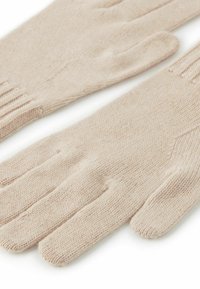 Beżowe rękawiczki z dzianiny o miękkiej teksturze, z czterema palcami, kciukiem i prążkowanymi mankietami na nadgarstkach. Prosty wzór, bez zdobień i elementów metalowych.