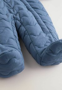 Blauer, gesteppten Schneeanzug mit einer weichen, strukturierten Oberfläche, der abgerundete Fußöffnungen und ein gewelltes gesticktes Muster entlang der Nähte aufweist.