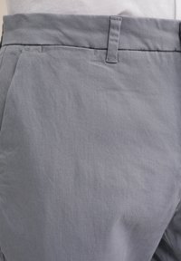 Pantaloni in tessuto leggero grigio con una texture liscia, dotati di una vita a taglio diritto, tasche laterali e una cintura su misura.