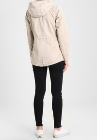 Beżowa kurtka z kapturem z wciągniętą talią, o teksturowanej strukturze i luźnym kroju. Połączona z czarnymi obcisłymi dżinsami i białymi trampkami.
