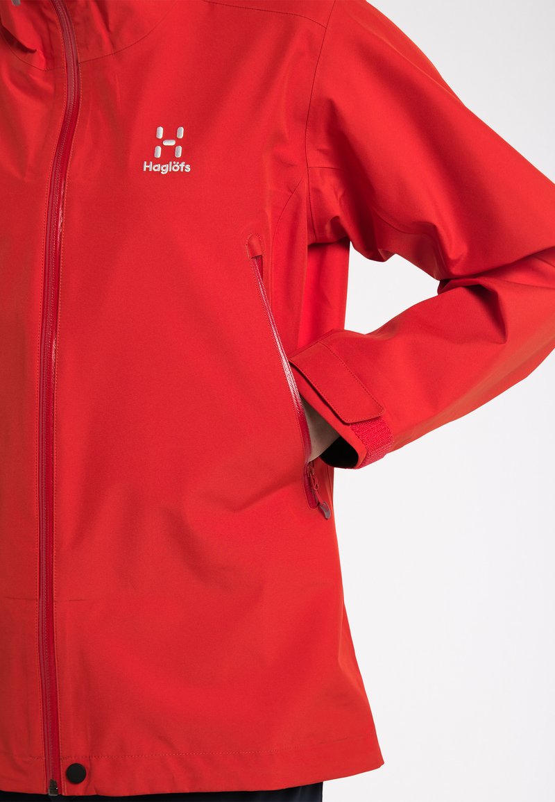 Červená voděodolná bunda se zapínáním na zip, s logem, bočními kapsami a nastavitelnými manžetami. Hladký povrch a přiléhavý střih.