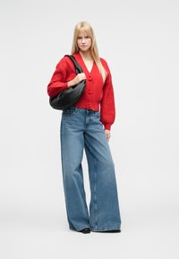 Sarkans adīts kardigans ar lielām pogām, koplektā ar platām zilā džinsa biksēm. Aksesuāri melna plecu soma. Gludas tekstūras, brīvs piegriezums.