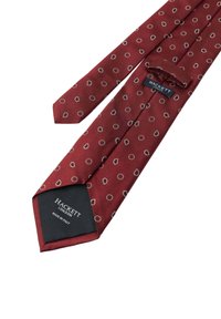 Burgundyslips med en texturerad tyg som har cirkulära mönster i guld och svart. Inkluderar en etikett med "HACKETT LONDON" och "MADE IN ITALY."