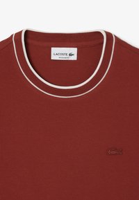 Maglietta in cotone rossa con collo a girocollo ribbed bianco, dotata di logo Lacoste ricamato nell'angolo in basso a sinistra e design a vestibilità regolare.