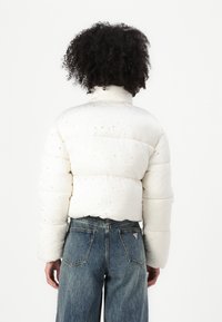 Giacca a vento bianca con colletto alto, caratterizzata da un design trapuntato e piccole finiture in argento. Abbinata a jeans in denim blu a vita alta.