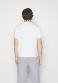 Witte T-shirt met korte mouwen en een ronde hals, gemaakt van zachte katoen; gedragen met lichtgrijze trainingsbroek.