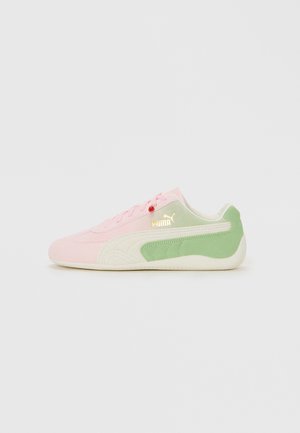 Baskets Puma profil bas avec tige rose, bande blanche, talon vert et logo Puma doré sur un fond clair.