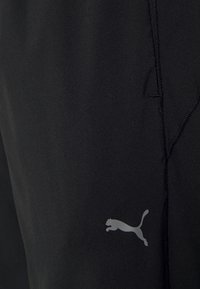 Schwarze Sportshorts mit glatter Textur, ausgestattet mit einem reflektierenden grauen Puma-Logo. Verstärkte Nähedetails entlang der Nähte.