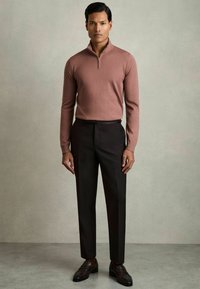Pullover in rosa polveroso, con zip; aderente. Pantaloni scuri; stile sartoriale. Mocassini in pelle marrone con un leggero lucido. Texture complessiva liscia.