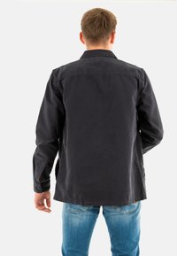 Donkerblauwe jas met kraag, knoopmanchetten en een relaxte pasvorm. Draag het over lichtblauwe jeans, die een stevige textuur tonen.