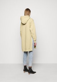 Sweat-shirt à capuche long de couleur jaune clair, avec fentes latérales, associé à un jean bleu clair et des bottines noires à talon carré.