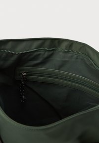 Interior de una bolsa de tela verde con una textura suave. Incluye un bolsillo con cremallera y costuras overlock a lo largo del borde superior.