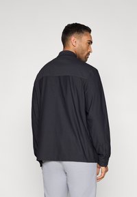 Σκούρο πουκάμισο με κουμπιά και μακριά μανίκια, με ελαφρώς υφασμένο ύφασμα και αντίθετη πάνελ στους ώμους. Σχεδιασμένο για άνετη εφαρμογή.