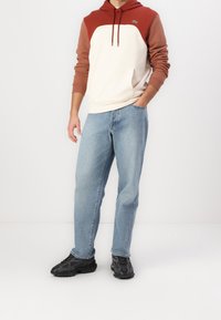 Sudadera con capucha de cuerpo crema y mangas color óxido, combinada con jeans de color azul claro y zapatillas deportivas negras.