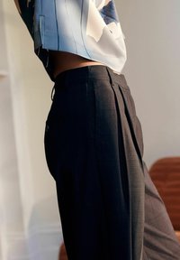 Pantaloni a quadri neri con pince, caratterizzati da una vestibilità sartoriale e una texture liscia. Abbinati a una blusa a maniche corte di colore azzurro chiaro.