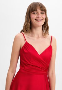 Rotes Kleid mit V-Ausschnitt und dünnen Trägern, das ein Wickeldesign aufweist und aus glattem, glänzendem Stoff gefertigt ist. Keine Muster oder Verzierungen sichtbar.