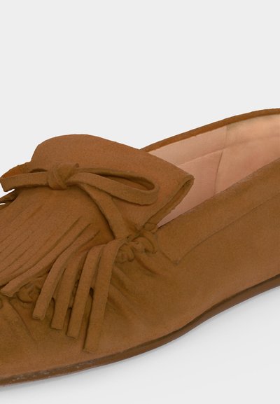 Mocassin en daim marron avec franges et détail de nœud, intérieur doux et rembourré, talon bas, présenté légèrement de biais sur fond blanc.
