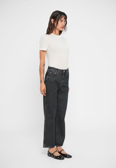 Zwarte high-waisted jeans met een rechte pijp, gecombineerd met een getailleerd wit T-shirt en zwarte flats met zilveren accenten.